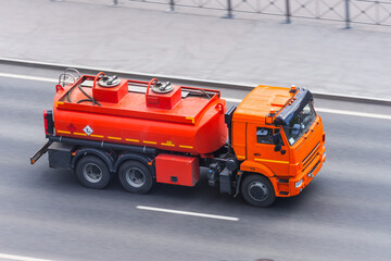 A bright orange truck with a tank for combustible fuel and other flammable liquids is driving along the highway.
