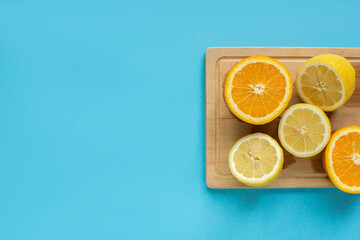top view of ripe cut lemon and orange on wooden cutting board on blue background