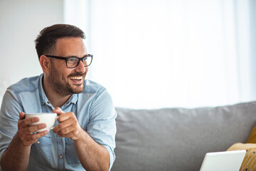 Man relaxing at home on the couch and having a coffee break, he is smiling and holding a cup....
