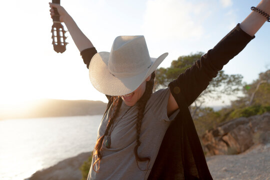 Wanderlust concept o woman with a cowboy look traveling with her guitar, the girl is wearing a hat and the evening light shines in the sky. The woman has views of the Mediterranean Sea Majorca Island