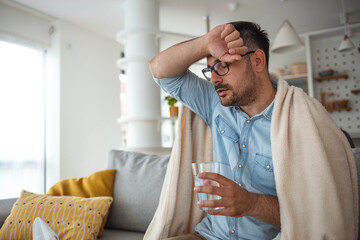 Cropped shot of a young man suffering with flu while sitting wrapped in a blanket on the sofa at...