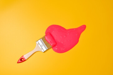 Shot of a brush with pink sticky slime on yellow background. Minimalism in photography, concept creative picture.