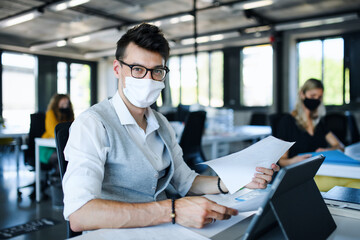 Portrait of young man with face mask back at work in office after lockdown.