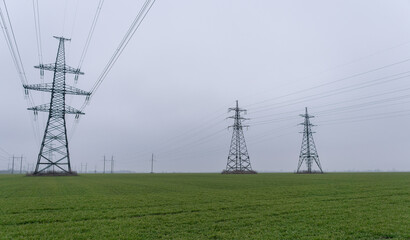 Electric network of pylons against a cloudy sky and a green meadow