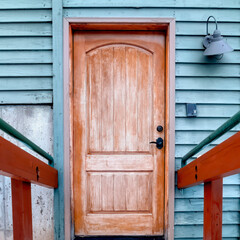 Square crop Snow covered stairs leading to brown wooden door of building with blue wall