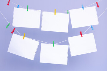 six white sheets of paper from a notepad on colorful clothespins on a clothesline. against a background of blue grainy paper.