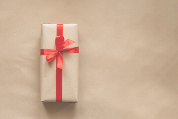 present wrapped in plain recycled paper with red ribbon on beige background