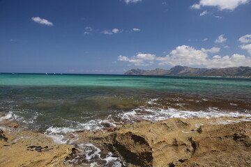 panorama landscape scenic view of isolated deserted yellow rocky beach with blue turquoise sea water and sky with white clouds and mountain background on beautiful and colorful Mallorca island, Spain