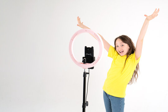 A teenage girl dances and shoots a video. Selfies. The phone is mounted on a tripod and the ring lamp shines. Emotion of delight and joy on the face of a child