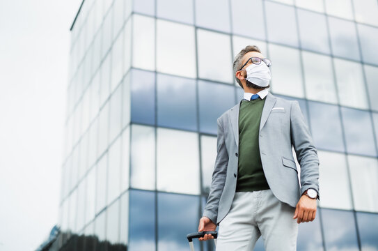 Businessman with luggage going on business trip, wearing face mask at the airport.