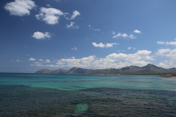 panorama landscape scenic view of blue sea water with underwater rocks and sky with white clouds and mountain background on beautiful and colorful Mallorca island in Spain