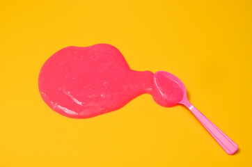 Shot of a blue plastic spoon with pink sticky slime on yellow background. Minimalism in photography, concept creative picture.