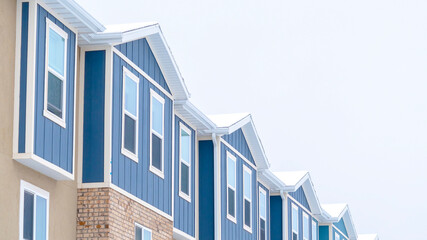 Panorama Snowy gable roofs at the facade of townhome with brick wall and vertical siding