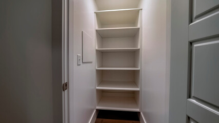 Panorama Walk in closet or pantry with empty wall shelves seen through open hinged door
