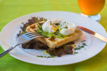Healthy breakfast on a terrace with Viennese waffles and poached egg with green salad and orange juice.