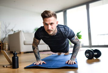 Front view portrait of man with tablet doing workout exercise indoors at home.