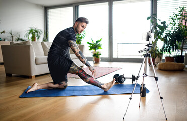 Man trainer doing online workout exercise indoors at home, using camera.