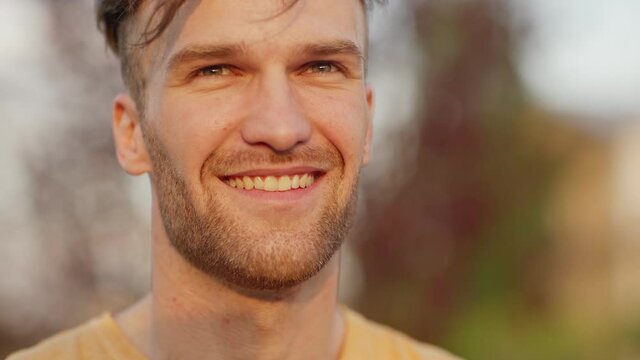Closeup portrait of handsome young man with stubble reading text message on cell phone, looking away and smiling standing outdoors in park