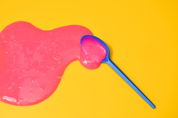 Shot of a blue plastic spoon with pink sticky slime on yellow background. Minimalism in photography, concept creative picture.