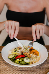 Fit woman in black top holding fork and knife eating vegan meal in a cafe close up. Middle aged woman with a plate of vegan dish in a restaurant alone. Social distancing. Healthy food and lifestyle.
