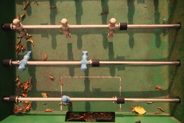 Top-shot on a green, highly weathered and leaf covered table football with its blue and brown figures casting long shadows in the surface in an autumn scenery