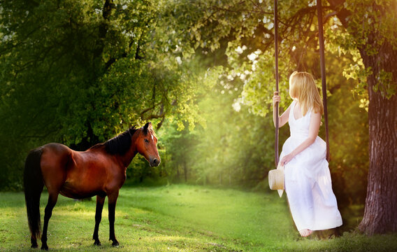 A girl in a white dress rides on a swing in nature and the horse grazes in the meadow. Pastoral paradise picture.