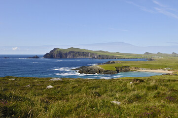 Vue sur la Baie de Dingle, ses champs, ses collines, ses falaises, ses rochers et sa verdure se d&eacute;tachant sur un ciel bleu et une mer indigo.