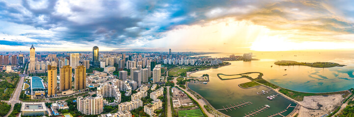 Fototapeta na wymiar China Hainan Haikou Cityscape in the Binhai Avenue CBD Area, with Landmark Buildings , Sea Port and Evergreen Park View During Sunset. Aerial View..