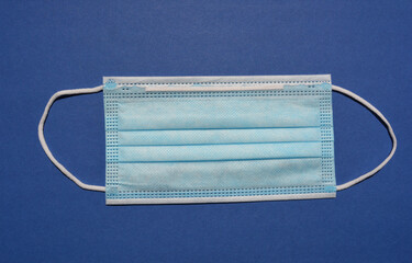 Disposable 3 ply non-surgical face mask with elastic ear loops isolated on blue background