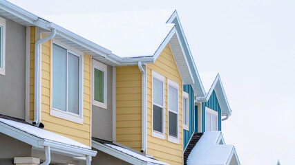Panorama crop Townhome exterior with snowy gable valley roof against overcast sky in winter