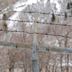 Square Focus on security chain link fence with barbed wires against on snowy hill slope