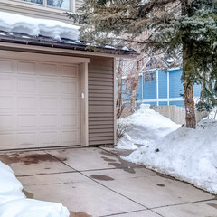 Square White garage door entrance of home with snow covered roof and yard in winter