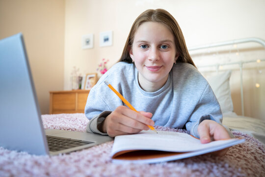 Portrait Of Teenage Girl Lying On Bed In Bedroom With Laptop Studying And Home Schooling