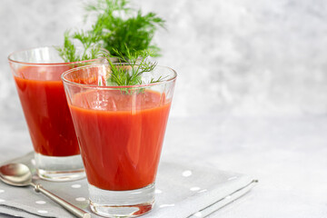 Tomato juice in glass cups. On a light gray background. Vitamin drink. Garnished with sprigs of dill.