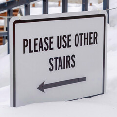 Square Stairs buried in winter snow with sign that reads Please Use Other Stairs