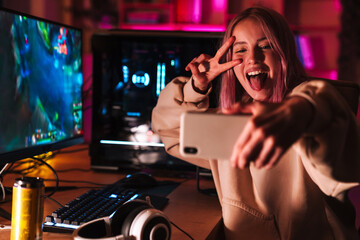 Image of girl taking selfie on cellphone while playing video game