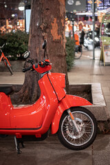 Bright Red Scooter parked In An Urban Street on a sidewalk under the tree