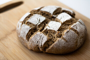 Homemade yeast sourdough rye wholegrain bread with Diamond Crosshatch scoring pattern on a wooden board with a kitchen towel. A dark and moody rustic atmosphere