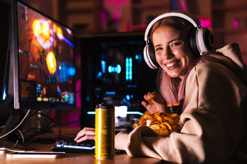 Image of cheerful cute girl eating chips while playing video game