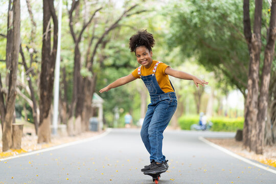 African American young girl having fun riding skateboard at summer outdoor. Teenager girl practicing skateboarding in the park.