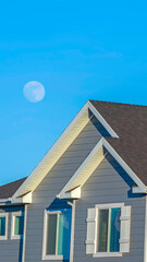Vertical crop Sunlit home with dark pitched roof over horizontal gray wall siding and windows
