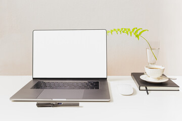 Mockup of laptop with mouse and pen with coffee cup over notebook on white table.