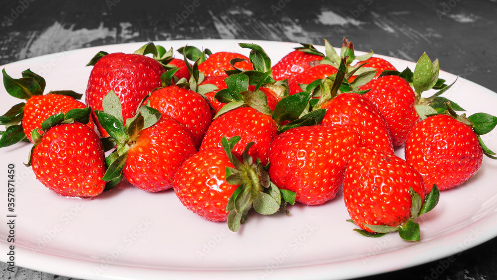 Wall mural a lot of ripe red strawberries in a white plate on a wooden table.