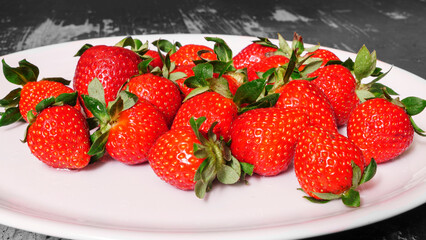 A lot of ripe red strawberries in a white plate on a wooden table.