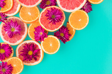 Colorful pattern composition made of slices of citrus fruits (orange, grapefruit) with purple flowers  in a turquoise background