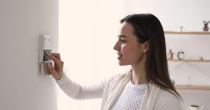 Happy young woman pressing buttons, activating apartment alarms system before leaving home. Smiling female client homeowner feelings safety, setting smart house security, easy technology concept.