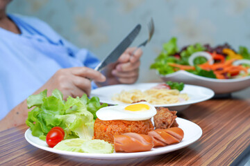 Asian senior or elderly old lady woman patient eating breakfast vegetable healthy food with hope and happy while sitting and hungry on bed in hospital.
