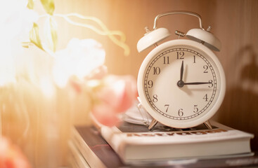 Classic white clock on the pile of books on the wooden backdrop for show the timing of life and...