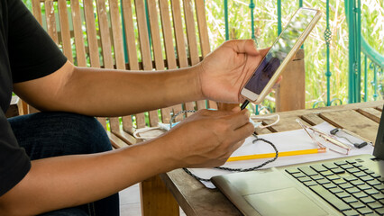 A woman is plugging in a charger cable into her smartphone in the office at home.