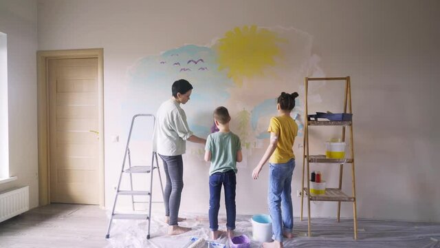 concentrated mother helps children to colour flat wall after relocation drawing images for kids birthday present during self isolation school holidays